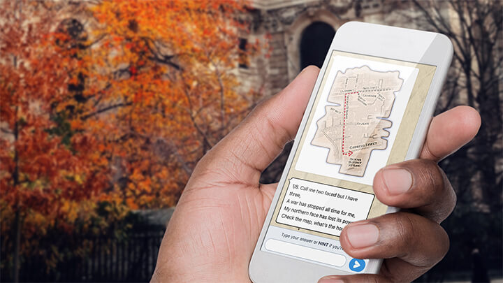 A hand holding a phone playing Treasure Hunt Nottingham with a tree with orange leaves behind.